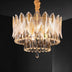 Round crystal chandelier with layered leaf-shaped amber glass panels and gold hardware suspended against a dark ceiling.