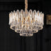 Crystal chandelier with gold accents and layered glass leaves hanging against a dark background.