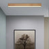 Rectangular wooden ceiling light with warm glow mounted above a framed tree photograph on a gray wall.