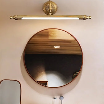 "A vintage-inspired wall lamp with a sleek, elongated bar and intricate detailing, illuminating a round bathroom mirror."