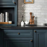 "Vintage brass flower-shaped knobs with bold, rounded petals, installed on dark blue kitchen cabinets, complementing the gray tiled backsplash and wooden countertop accessories."
