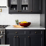 "Vintage brass flower-shaped knobs with bold, rounded petals, installed on dark gray kitchen cabinets, complementing the white countertop and backsplash."