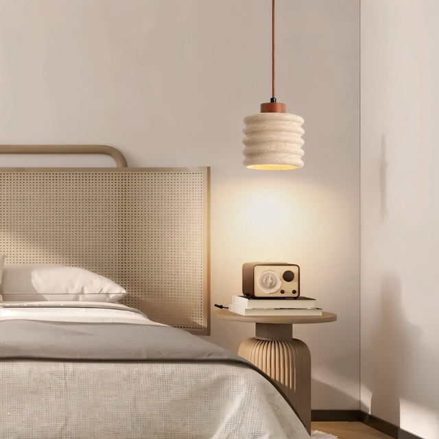 "A travertine pendant light with a ribbed design hanging over a bedside table with a radio in a bedroom."