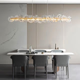 "A linear chandelier with sculpted glass petals and an iron frame in a dining room."