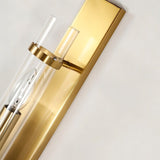 "Close-up of a modern brass wall lamp with a rectangular base and a cylindrical glass shade, showing the light bulb inside."