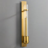 "A modern brass wall lamp with a rectangular base and a cylindrical glass shade mounted on a gray wall."