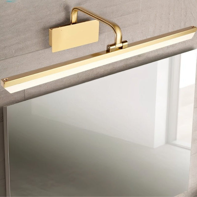 "A gold-finish LED vanity light mounted above a bathroom mirror with a polished surface."