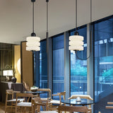 "Modern pendant lights with layered frosted glass diffusers and black iron frames, hanging in a cafe setting."
