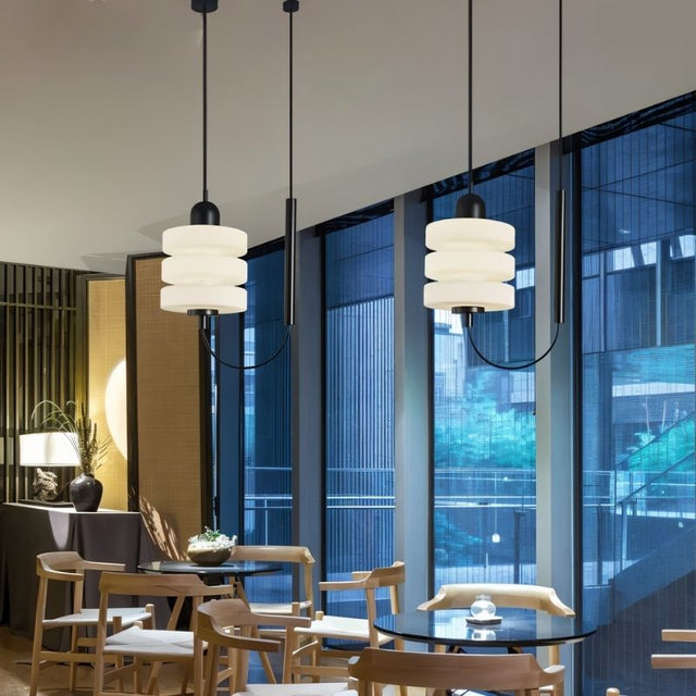 "Modern pendant lights with layered frosted glass diffusers and black iron frames, hanging in a cafe setting."