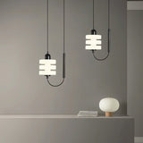 "Pair of modern pendant lights with layered frosted glass diffusers and black iron frames, hanging above a shelf."