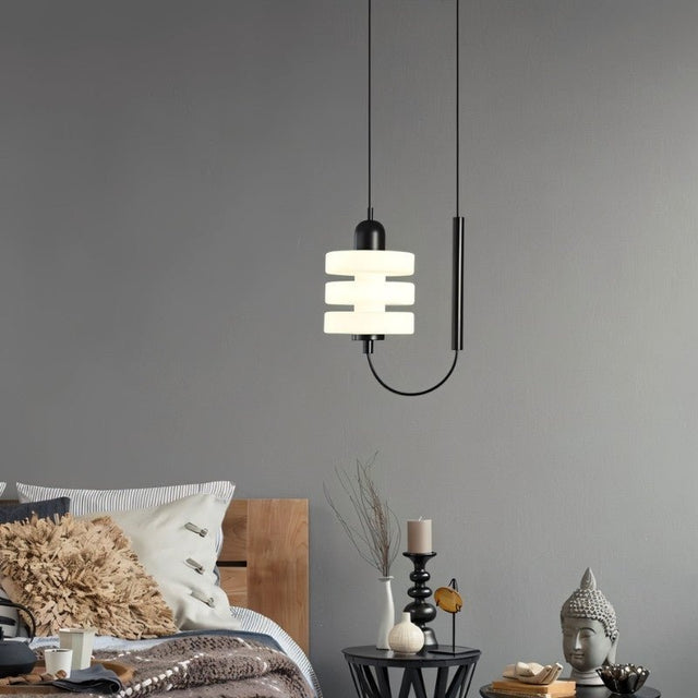 "Modern pendant light with a layered frosted glass diffuser and black iron frame, hanging in a bedroom."
