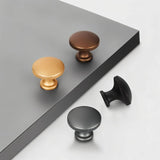 "A set of minimalist cabinet knobs in various metallic finishes, arranged on a grey and white surface."