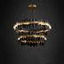 Tiered round chandelier with brass rings and black hanging crystal prisms suspended against a dark background.