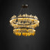 Tiered round chandelier with gold-leaf fringe details and brushed metal rings suspended against a dark background.