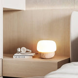 "Minimalist table lamp with a travertine base and glass shade on a wooden nightstand"