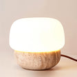 "Modern table lamp with a natural travertine base and a softly glowing glass diffuser"