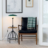 "Nisra Table Lamp with a vibrant green top shade and frosted glass diffuser, placed beside a comfortable chair in a modern living room, crafted from aluminum, iron, and glass."