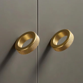 "Two gold brass cylindrical knobs with knurled texture on a dark gray cabinet."