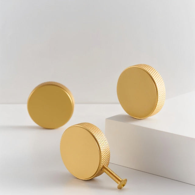 "Three gold brass cylindrical knobs with knurled texture on a white and gray background, showcasing a modern design."