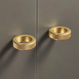 "Two gold brass cylindrical knobs with knurled texture on a dark gray cabinet door."