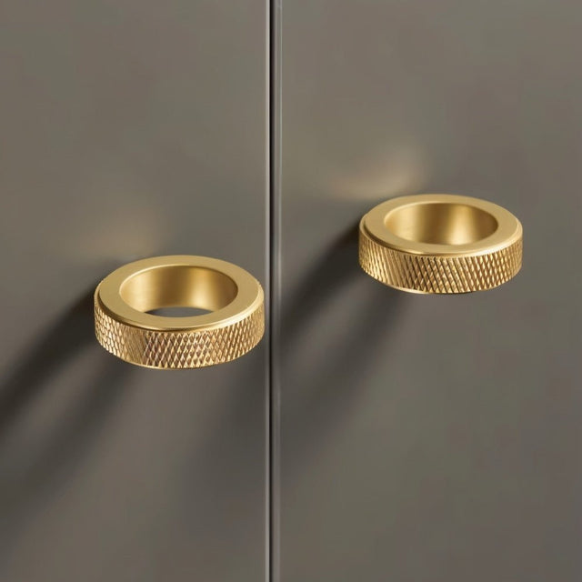 "Two gold brass cylindrical knobs with knurled texture on a dark gray cabinet door."