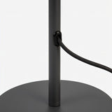 "A close-up view of the black base and cord of a white table lamp with a layered, wave-like diffuser."