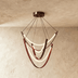Multi-tiered pendant light with curved red leather straps and illuminated white rings, suspended from bronze canopy against w