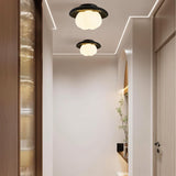 "Two ceiling lights with black travertine frames and cloud-shaped acrylic shades, illuminating a hallway with wooden doors and trim."