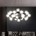 Modern chandelier with clear glass spheres and black metal frame suspended above gray tufted sofa against dark wall.