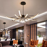 "A black chandelier with twelve curved branches, each tipped with a white light, installed in a large modern living room with a second matching chandelier visible in the background."
