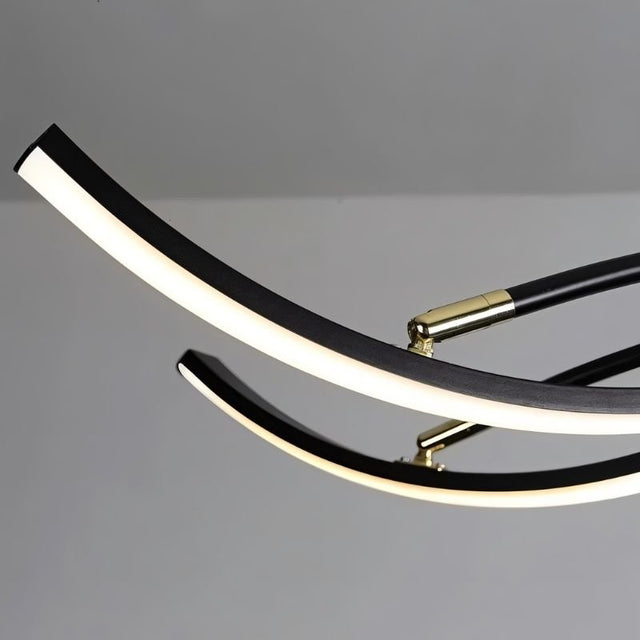 "A close-up view of the Nyralis Chandelier, showing a curved black arm with a white light strip and brass connector against a gray background."