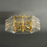 "An angled view of a modern flush mount ceiling light with a geometric glass shade and gold frame, against a dark background."