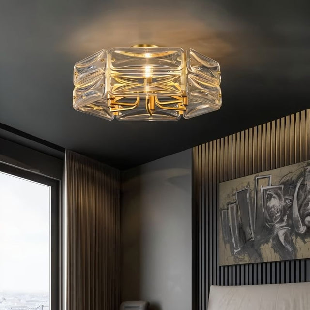 "A modern flush mount ceiling light with a geometric glass shade and gold frame, installed in a bedroom with artwork and curtains."