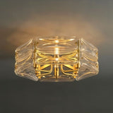 "A close-up view of a modern flush mount ceiling light with a geometric glass shade and gold frame, illuminated against a dark background."