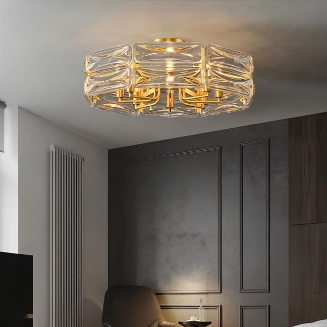 "A modern flush mount ceiling light with a geometric glass shade and gold frame, installed in a living room with a chair and radiator."