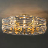 "A modern flush mount ceiling light with a geometric glass shade and gold frame, illuminated against a dark background."