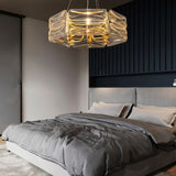 "A modern round chandelier with a geometric glass shade and gold frame, hanging above a bed in a bedroom with gray bedding."