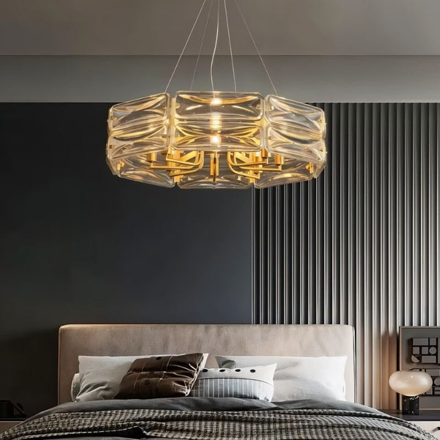 "A modern round chandelier with a geometric glass shade and gold frame, hanging in a bedroom."
