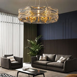 "A modern round chandelier with a geometric glass shade and gold frame, hanging in a living room with a gray couch and armchair."