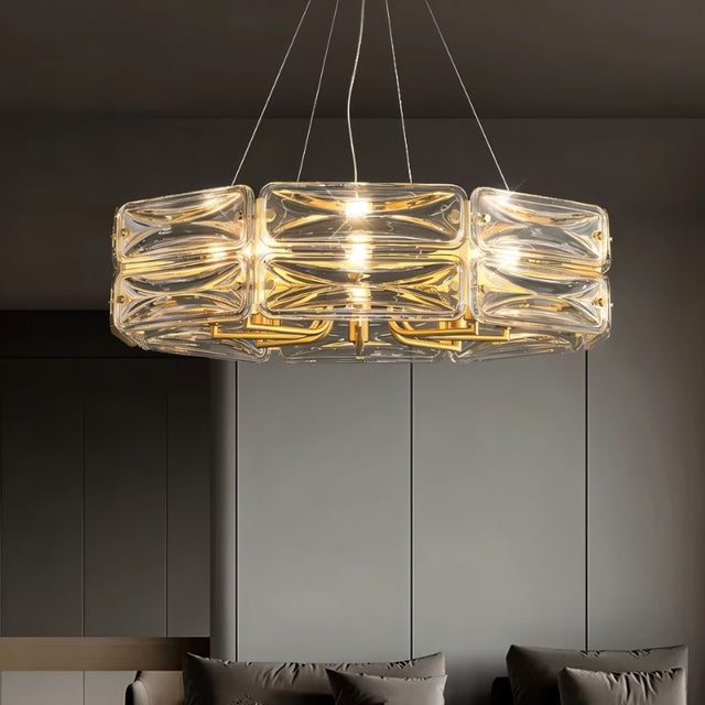 "A modern round chandelier with a geometric glass shade and gold frame, hanging in a living room with a couch."