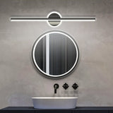 "A modern black wall lamp with a cylindrical bar intersecting a circular base, mounted above a round mirror in a contemporary bathroom with a white vessel sink and gray walls."