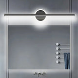 "A modern black wall lamp with a cylindrical bar intersecting a circular base, mounted above a rectangular mirror in a contemporary bathroom with a gray tiled wall and a towel rack."