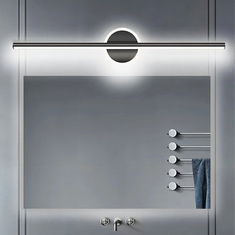 "A modern black wall lamp with a cylindrical bar intersecting a circular base, mounted above a rectangular mirror in a contemporary bathroom with a gray tiled wall and a towel rack."