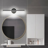 "A modern black wall lamp with a cylindrical bar intersecting a circular base, mounted above a round mirror in a contemporary bathroom with gray tiled walls."