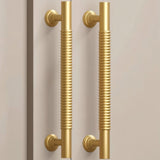 "Pair of solid brass pull bar handles with a grooved design on a light-colored cabinet."