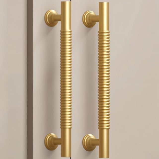 "Pair of solid brass pull bar handles with a grooved design on a light-colored cabinet."
