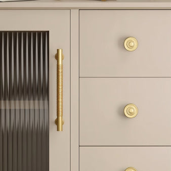 "Solid brass knobs and a pull bar with a grooved design on a light grey cabinet with textured glass."