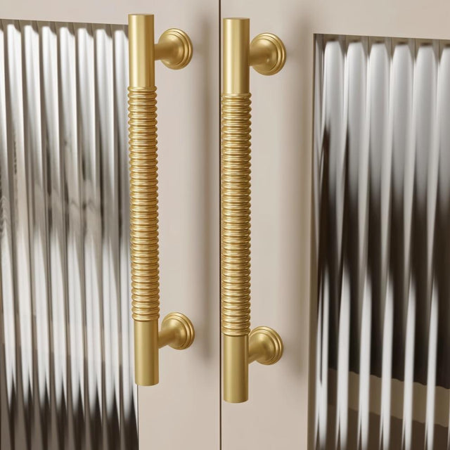 "Pair of solid brass pull bars with a grooved design on a glass cabinet with textured doors."