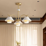 "A modern brass chandelier with three textured ceramic shades in a room with sheer curtains."
