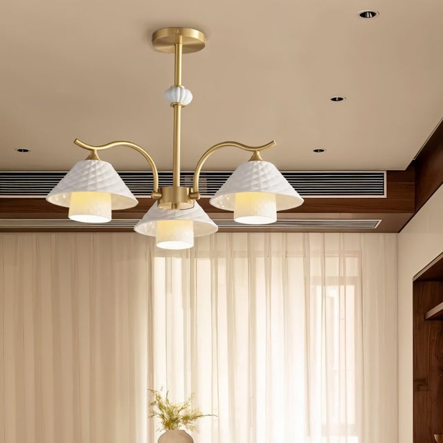 "A modern brass chandelier with three textured ceramic shades in a room with sheer curtains."